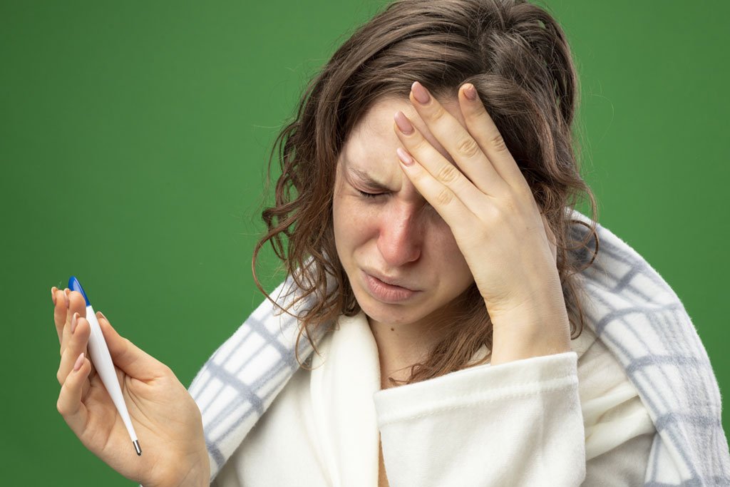 Woman checking her temperature while feeling unwell